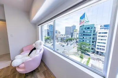 a teddy bear sitting in a pink chair looking out a window at Inn The Omotesando in Tokyo