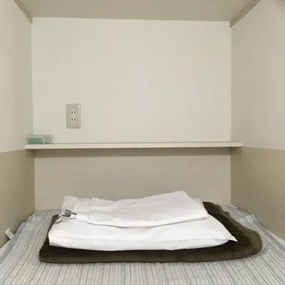 a bed with white sheets and a shelf on the wall at 1 Night 1980 Hostel Tokyo Asakusa Simple Stay in Tokyo