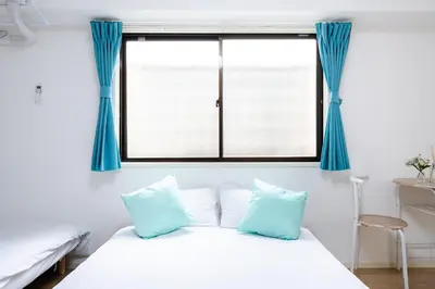 a white bed with blue curtains and a window at SUA HOTEL Nishikasai in Tokyo