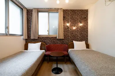a room with two beds and a red chair at City Oasis in Tokyo