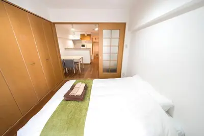 a bedroom with a large white bed and a kitchen at Shibuya E Address 303 in Tokyo