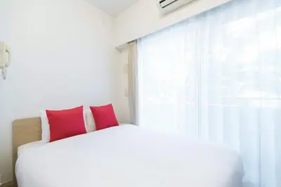 a white bed with red pillows next to a window at Ihatov Komazawa in Tokyo