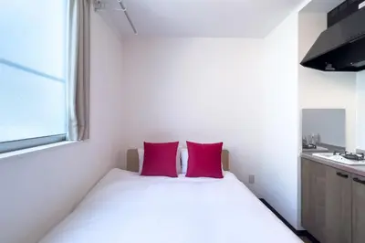 a small bedroom with a white bed with two red pillows at \u30a8\u30ec\u30ac\u30f3\u30c8\u30cf\u30a6\u30b9 in Tokyo