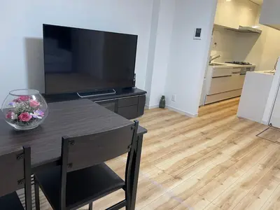 a living room with a table with a television and a kitchen at Private Hotel Season Spring in Tokyo