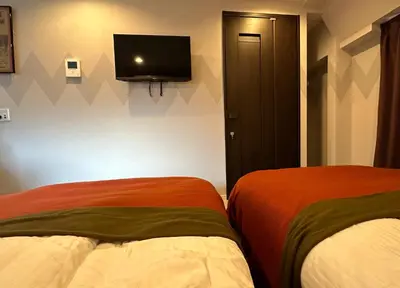 a bedroom with two beds and a tv on the wall at Hotel COMACHI in Tokyo