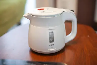 a white electric kettle sitting on a wooden table at \u6e0b\u8c37\u672c\u753a4\u4e01\u76ee\u6238\u5efa in Tokyo