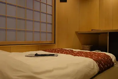 a bed in a room with a white blanket and a controller on it at \u4e07\u96f7\u30db\u30c6\u30eb in Tokyo