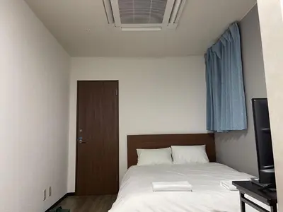 a bedroom with a bed with white sheets and a television at TokyoGuest Akihabara in Tokyo