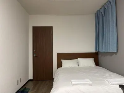 a bedroom with a bed with white sheets and a wooden door at TokyoGuest Akihabara in Tokyo