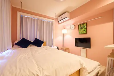 a bedroom with a white bed with a tv on the wall at Shinjuku colorbee pretty house103 in Tokyo
