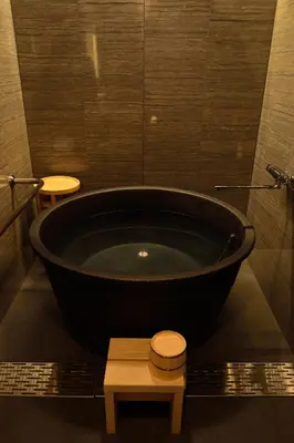 a black bath tub in a bathroom with two stools at Hotel Ryumeikan Ochanomizu Honten in Tokyo