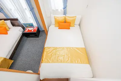 two beds in a small room with orange pillows at KYARA HOTEL \u4e80\u6238a in Tokyo