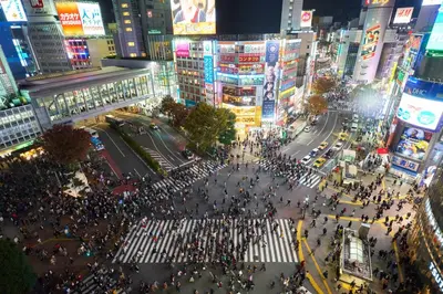a large crowd of people crossing a busy city street at illi Mani Shibuya in Tokyo