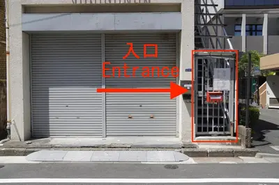 a no entrance sign on a garage door with an orange arrow at \u99c5\u5f92\u6b694\u5206 \u90fd\u5fc3\u306e\u5e83\u3005\u7a7a\u9593 \u5404\u968e\u8cb8\u5207 \u9280\u5ea7 \u304a\u53f0\u5834 \u8c4a\u6d32\u3059\u3050 \u7530\u753a \u4e09\u7530\u99c5\u3082\u5229\u7528\u53ef in Tokyo