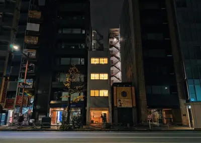 a tall building with lights on in a city at night at HERE.Tokyo in Tokyo