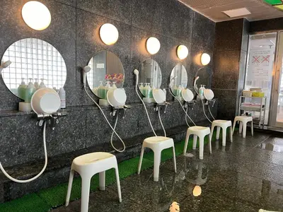 a row of mirrors on a wall with stools at 男性専用サウナ&カプセル Men Only Capsule Room & Sauna, Bathhouse ミナミ下北沢 Minami Shimokitazawa in Tokyo