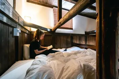 a woman sitting on a bed reading a book at Hotel Suzumeya Tsukiji \u30db\u30c6\u30eb\u3059\u305a\u3081\u3084\u7bc9\u5730 in Tokyo