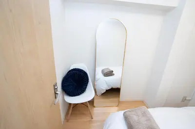 a bedroom with a mirror and a white chair with a blue pillow at \u82b1\u5bbf\u65b0\u5bbf HANAYADO SHINJUKU in Tokyo