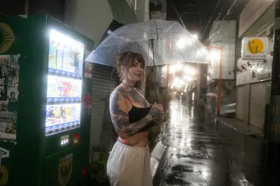 a woman is standing under an umbrella in the rain at Saku House Jujo in Tokyo