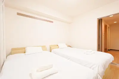two beds in a room with white sheets at Shinjuku Waseda Earthtone Apartment in Tokyo
