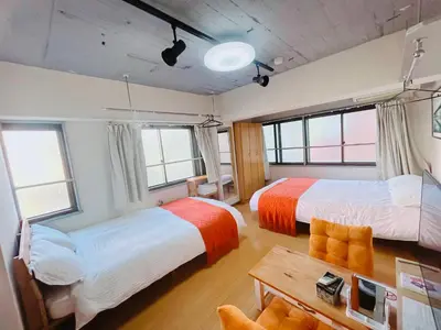 two beds in a room with windows and a table at Ueno Iriya Hotel in Tokyo