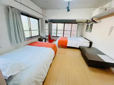 a bedroom with two beds and a table and windows at Ueno Iriya Hotel in Tokyo