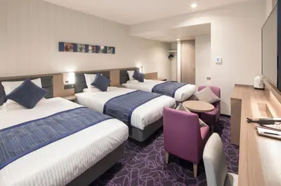a hotel room with three beds and a table and chairs at Hotel Mystays Gotanda Station in Tokyo