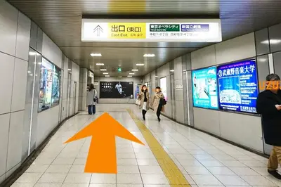 an arrow on a hallway with people walking in a subway at \u65b0\u5bbf\u307e\u30671\u99c5 \u521d\u53f0\u99c5\u5f92\u6b699\u5206 \u30b3\u30f3\u30d3\u30cb2\u5206 PokeMon\u3068\u66ae\u3089\u3059\u30c7\u30b6\u30a4\u30ca\u30fc\u30ba\u30eb\u30fc\u30e0 in Tokyo