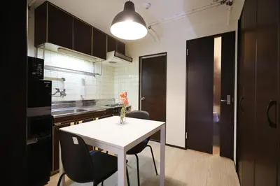 a kitchen with a white table and black cabinets at Shinjuku Kabukicho Harmony Inn in Tokyo