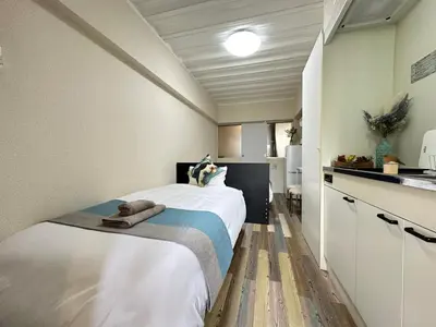 a bedroom with a large white bed and a kitchen at nestay inn tokyo waseda in Tokyo