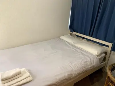 a small bed with a blue curtain and white sheets at \u30a2\u30f3\u30c9\u30b9\u30c6\u30a4\u30ce\u30dc\u30c3\u30c1\u30db\u30c6\u30ebn3 in Tokyo