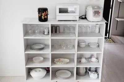 a white shelf filled with dishes and plates and a microwave at \u862d\u5712 Village Gotanda \u5c4b\u4e0a\u30ac\u30fc\u30c7\u30f3\u30c6\u30e9\u30b9\u4ed8\u304d in Tokyo