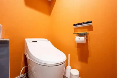 a bathroom with a white toilet in an orange wall at lighthouse otsuka in Tokyo