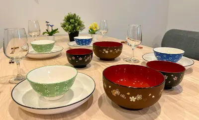 a wooden table with bowls and wine glasses on it at Brand New Modern Haven 7-Min Walk to Shinkoenji Station 9-Min Train to Shinjuku in Tokyo