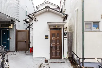 a small white building with a brown door at \u5f25\u751f\u753a1\u4e01\u76ee\u6238\u5efa in Tokyo