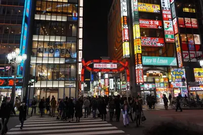 a crowd of people crossing a busy city street at night at \u65b0\u5bbf\u5e02\u4e2d\u5fc3\u6b4c\u821e\u4f0e\u5ba2\u623f\u6e90\u51fa\u884c\u4fbf\u5229\u514d\u8d39Wi-Fi in Tokyo