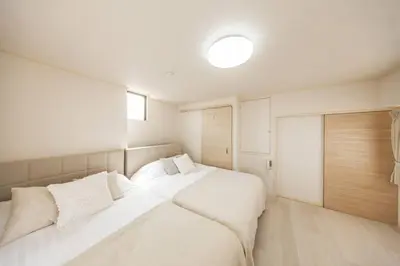 a white bedroom with two beds and a window at NewOpen! \u99c5\u5f92\u6b691\u5206 \u6c60\u888b\u30a8\u30ea\u30a2 60\u5e73\u7c73\u6700\u59278\u540d\u5bbf\u6cca\u53ef\u80fd \u548c\u98a8\u30e2\u30c0\u30f3 in Tokyo