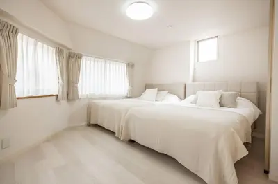 two beds in a white room with two windows at NewOpen! \u99c5\u5f92\u6b691\u5206 \u6c60\u888b\u30a8\u30ea\u30a2 60\u5e73\u7c73\u6700\u59278\u540d\u5bbf\u6cca\u53ef\u80fd \u548c\u98a8\u30e2\u30c0\u30f3 in Tokyo