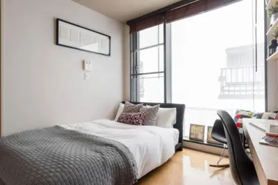 a bedroom with a bed and a desk and windows at EstLargo Meguro in Tokyo