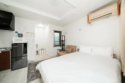 a bedroom with a white bed and a kitchen at Momo-stay Ikebukuro in Tokyo