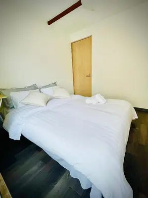 a large white bed with white sheets and a wooden door at RED House｜12 minutes from the station｜Quiet area｜Direct access to Shinjuku & Akihabara in Tokyo
