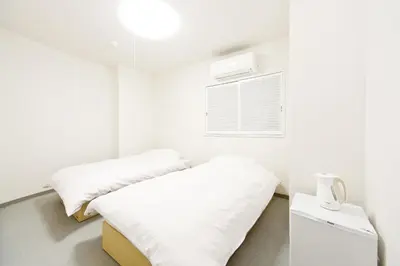 a white room with two beds and a window at Business Hotel Yamashiro in Tokyo