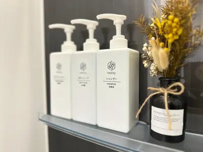 a shelf with three bottles of soap and a vase with flowers at nestay inn tokyo skytree in Tokyo