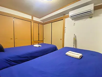a room with two beds with blue sheets and a fan at Ema eve HOUSE in Tokyo