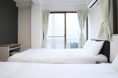 two beds in a hotel room with a window at MX House - Cozy APT Stay in Ikebukuro Tokyo, with Direct Access to Shinjuku & Shibuya in Tokyo