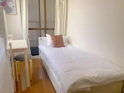a small bedroom with a white bed with a pink pillow at Mori house ookubobiru in Tokyo