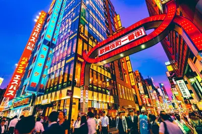 a crowd of people crossing a busy city street at night at Higashi-Shinjuku 904 in Tokyo