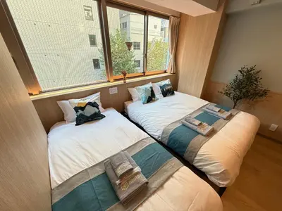 two beds in a small room with a window at nestay inn tokyo tsukiji in Tokyo