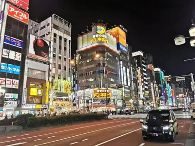 a city street at night with cars on the road at Shinjuku\u5bbf in Tokyo