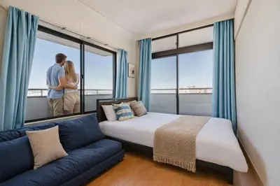 a couple standing in a room with a bed and a couch at 9th floor Elevator Yamanote Line Komagome Station 3 mins walk 3 rooms 1 room 1 room Direct access to Shinjuku Ueno Akihabara Ginza Tokyo Ikebukuro Shinjuku Shibu in Tokyo